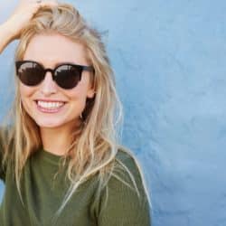 Close up shot of pretty young woman in sunglasses smiling. Attractive young female model with copy space on blue background